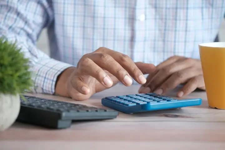 Hands working a calculator beside a laptop and notebook