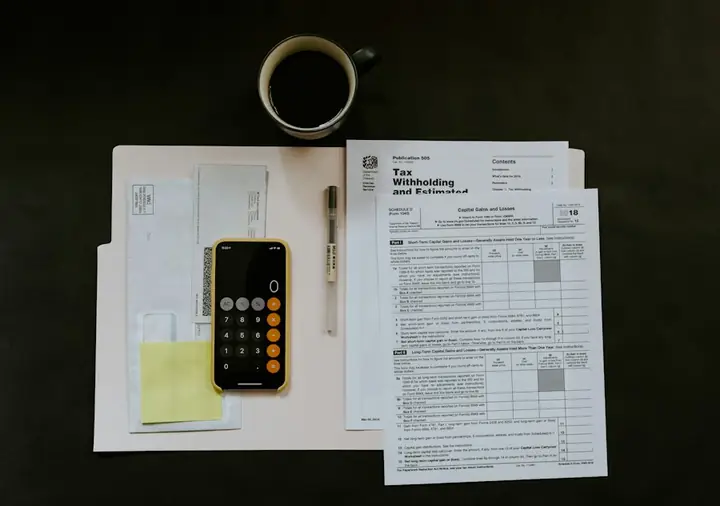 Tax forms, a phone calculator and a pen on a desk