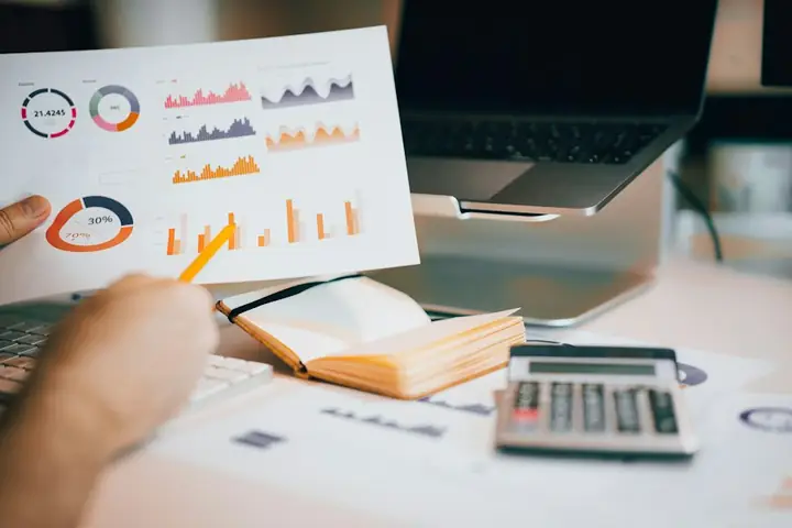 Printed financial charts held above a laptop